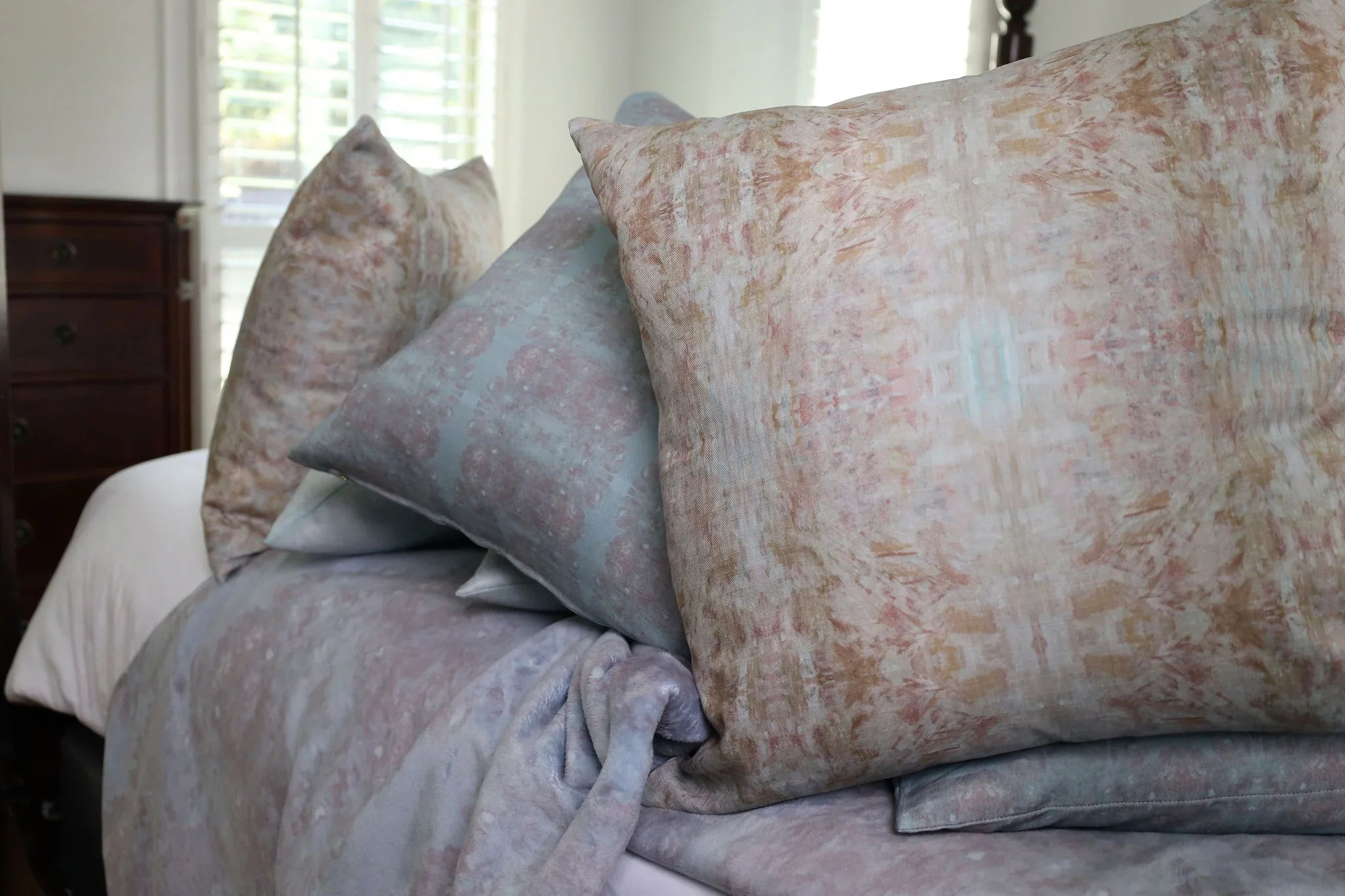 The Gardens Bronze Iris luxury decorative pillow featuring an abstract floral pattern with layered artistic movement and rich bronze, plum, and earthy tones, handcrafted in England for luxury living rooms, designer-curated interiors, thoughtfully layered spaces, and modern traditional homes.